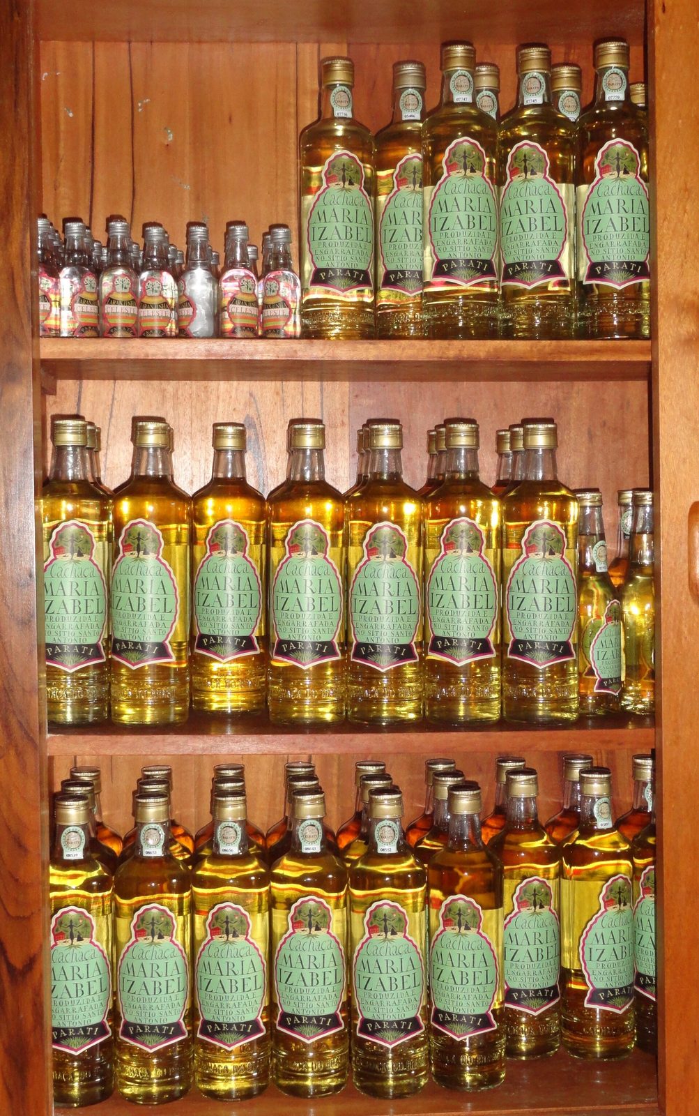 Shelves of artisanal cachaça at a Paraty distillery, from clear branca to bottles aged in native woods.