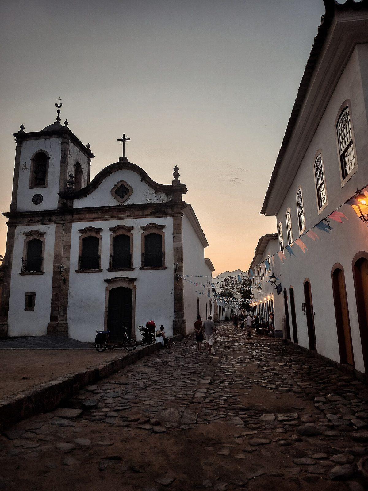 A Paraty church lit against the deep blue of dusk, when the crowds thin and the white walls glow over the empty streets.