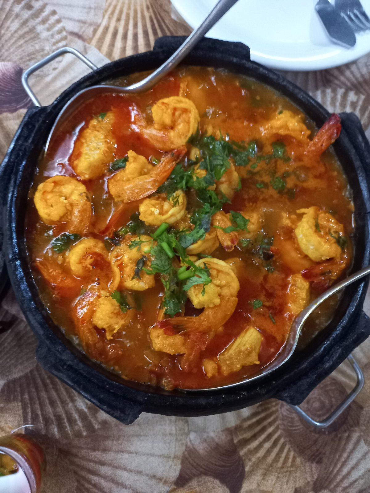 A shrimp stew brought to the table in a dark clay pot, still bubbling from the heat.