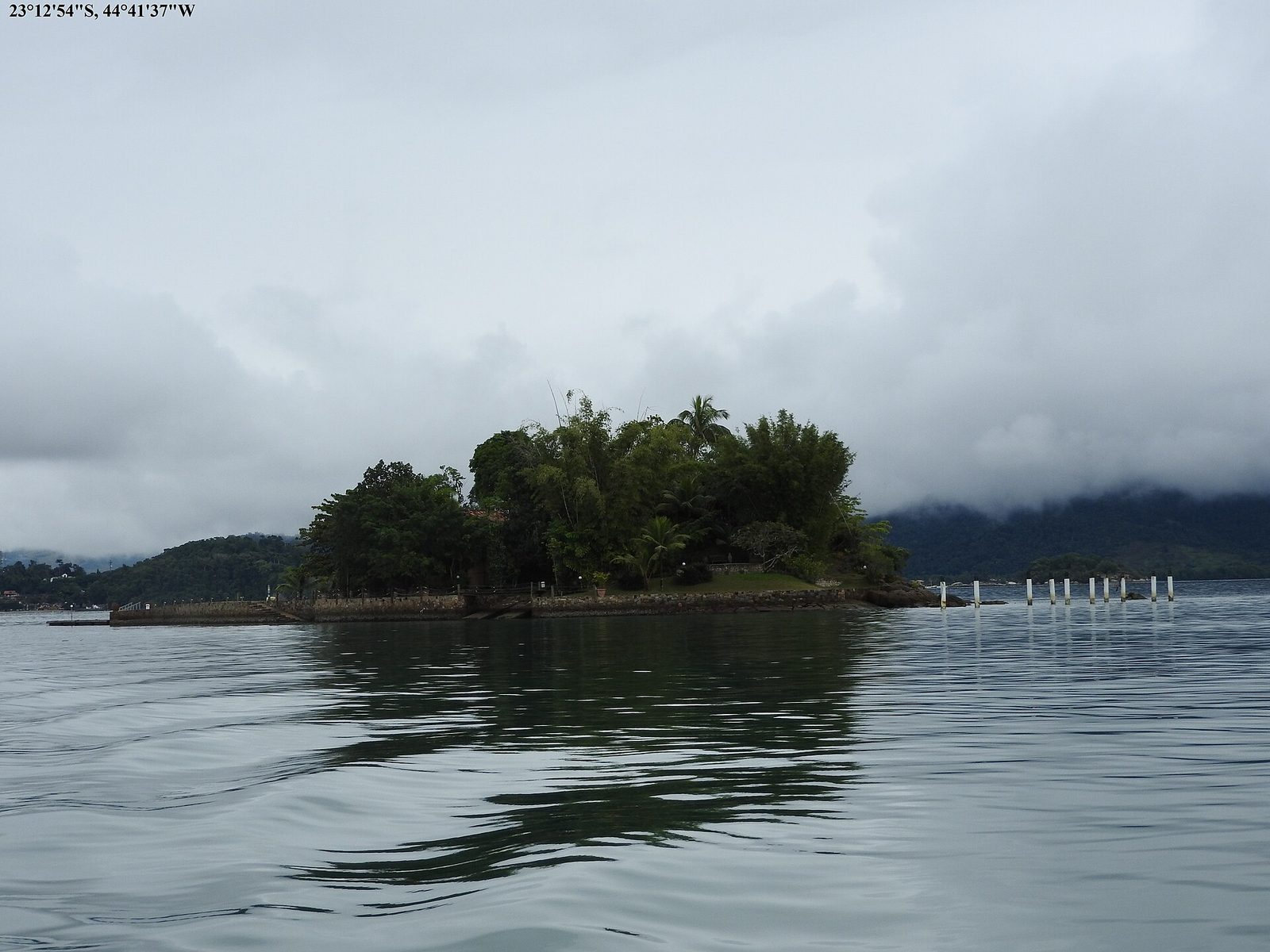 A lone forested island standing in soft mist, the rocky shallows around its edges the kind of place snorkelers head for.