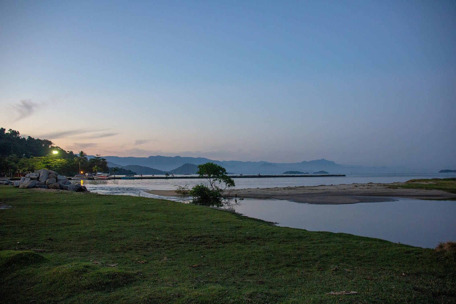 The bay lies still under a deep blue sky, the mountains fading into soft layers behind the water.