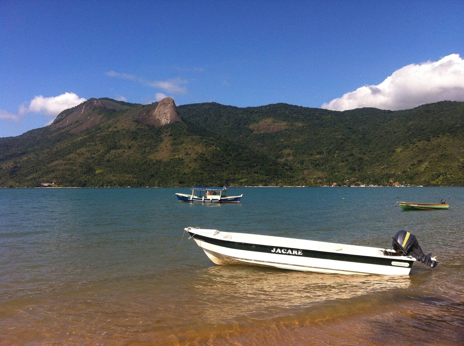 The long, narrow bay running back between forested ridges, with the Pico do Pão de Açúcar de Mamanguá standing over it and a single small boat for scale.