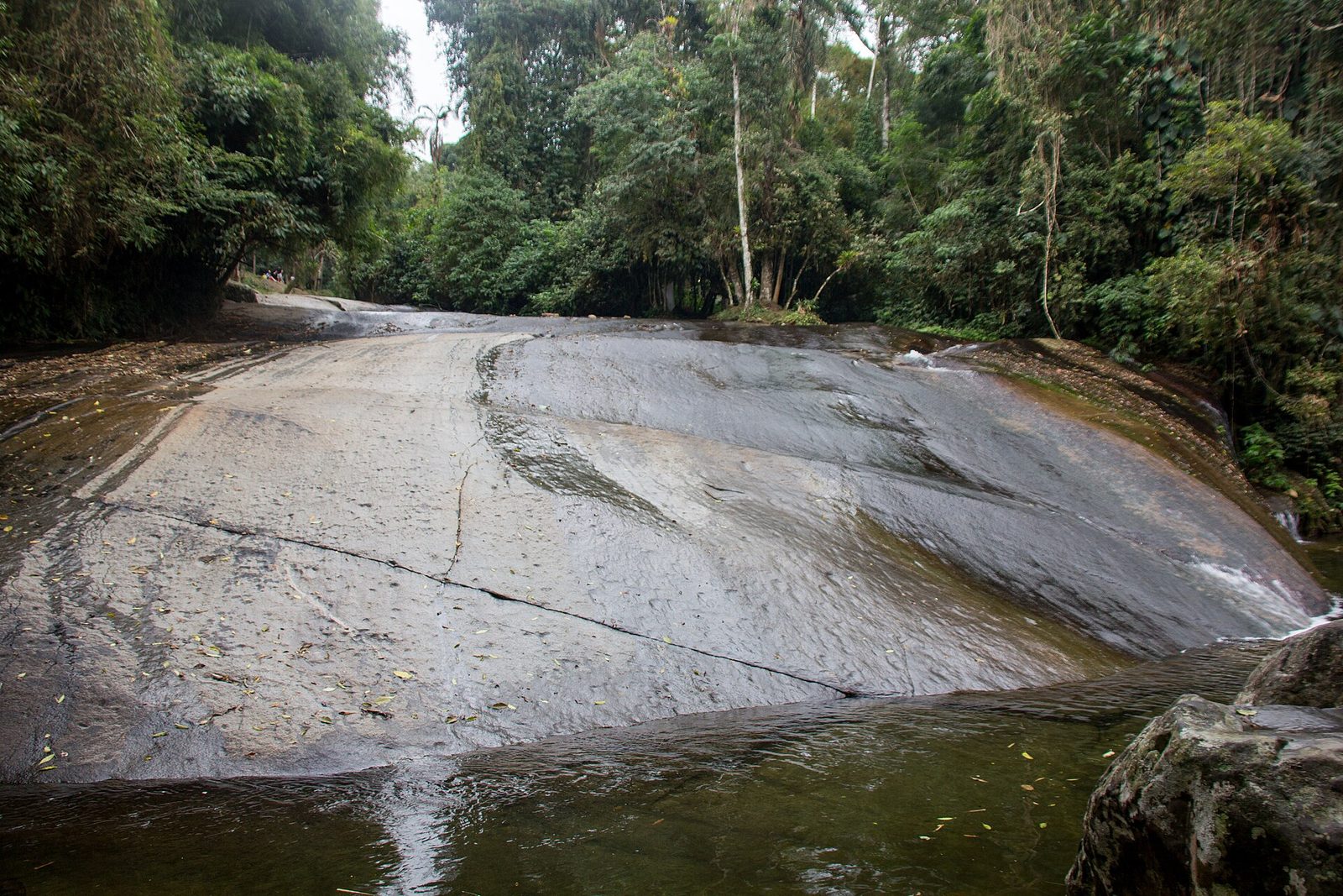 A river-polished granite chute of the kind Paraty is known for; the smooth rock carries sliders down into the pool at the base.